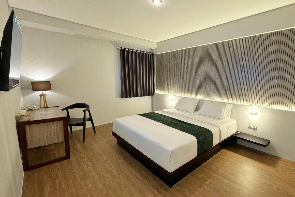 A modern hotel room with a neatly made bed, a desk with a lamp, and a chair.