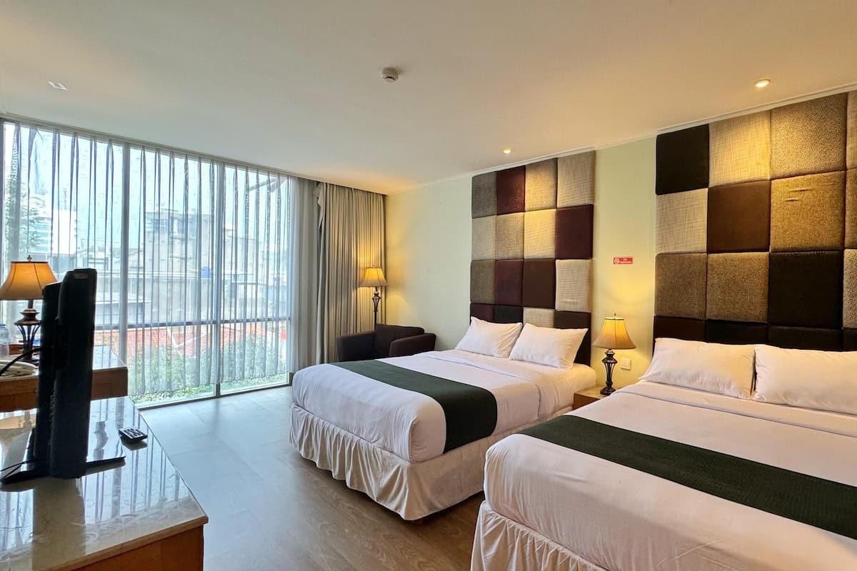 A hotel room with two beds, a desk, and a large window.