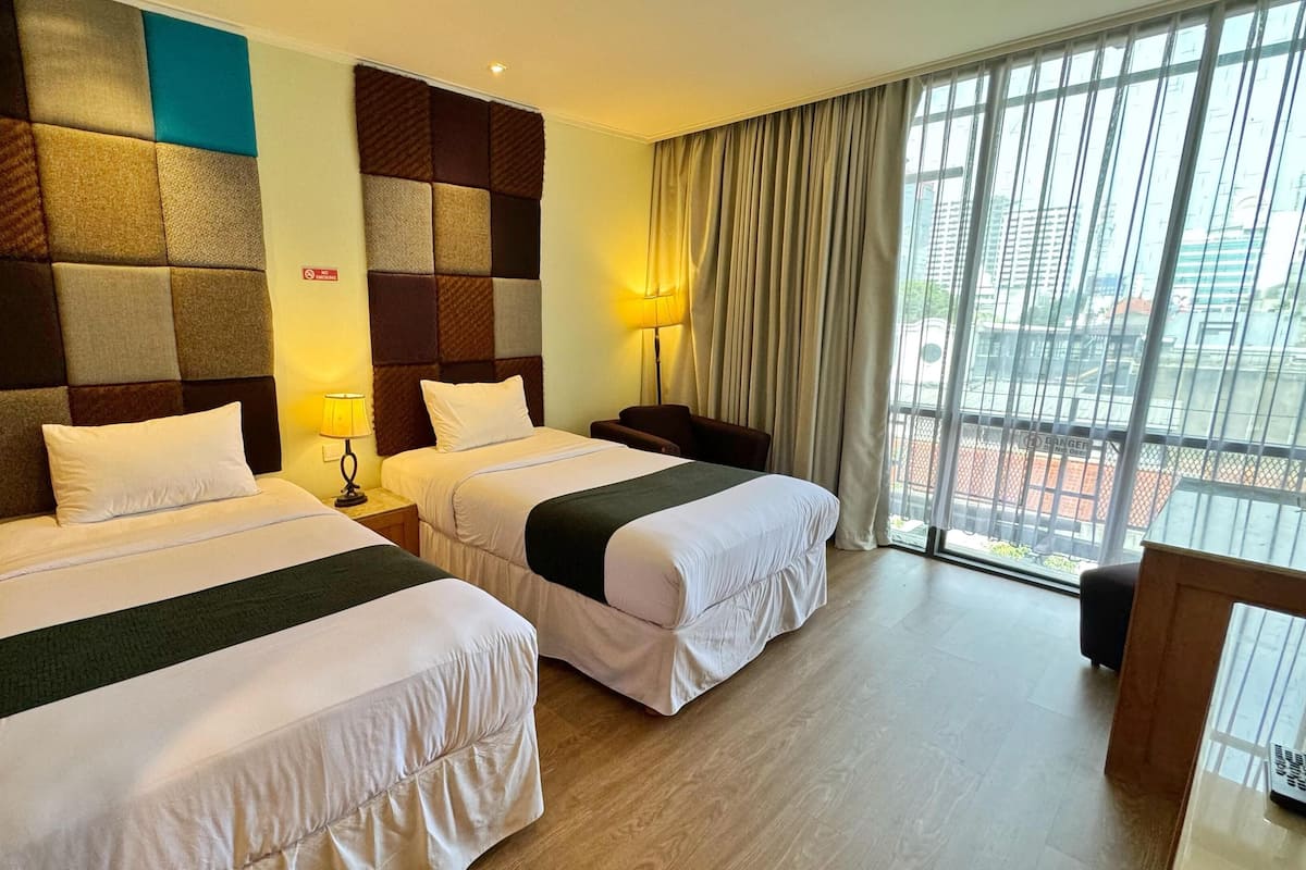 A hotel room with two beds, a large window with curtains, a view of the city, and a modern design.
