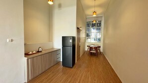 A narrow hallway with a wooden floor, a black refrigerator, a wooden cabinet, and a window with a view. - Chara Hotel (Bandung)
