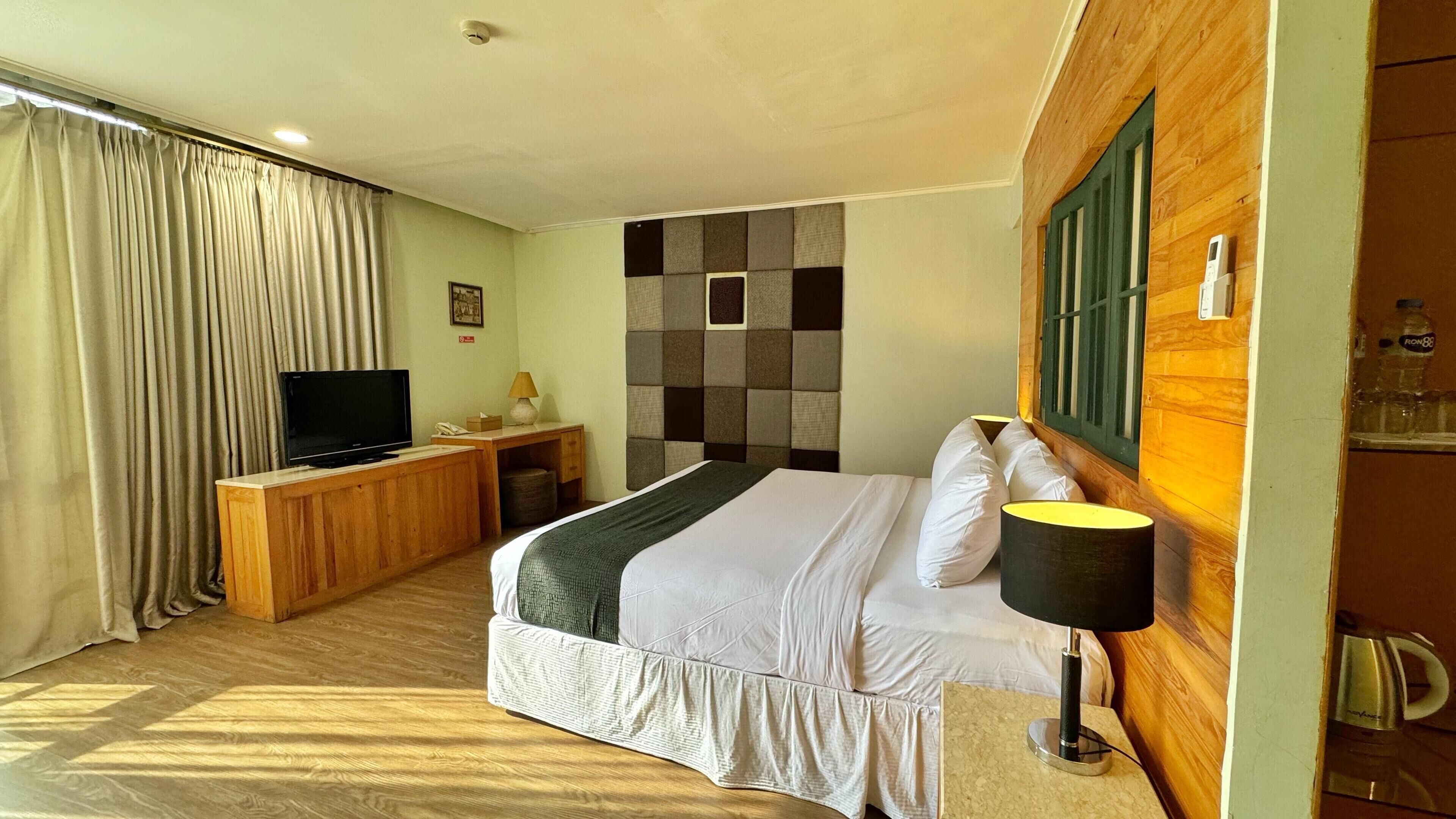 A hotel room with a bed, a television, a desk, and a window with curtains.