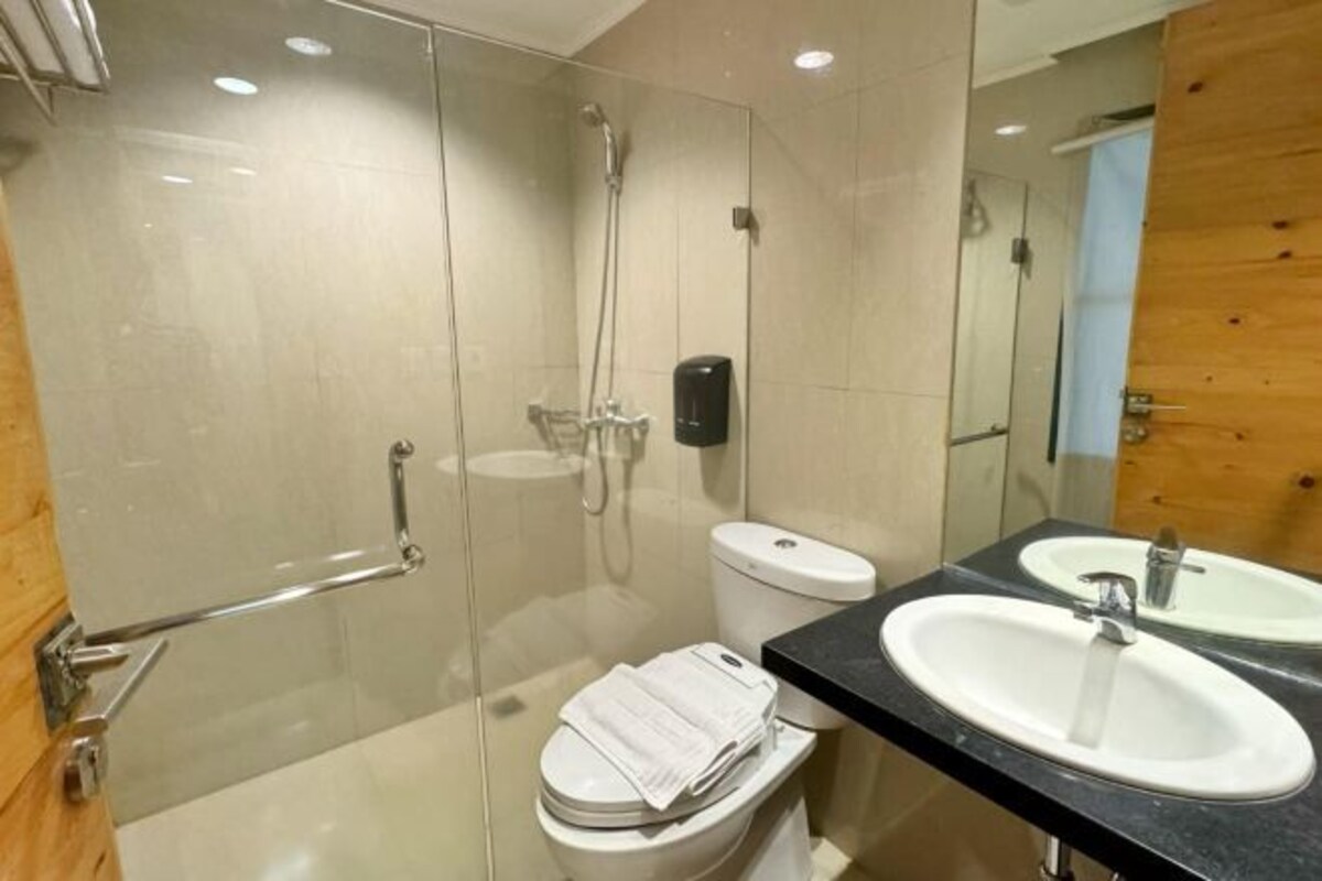 A modern bathroom with a glass shower enclosure, a toilet with a towel on it, and two sinks with mirrors.