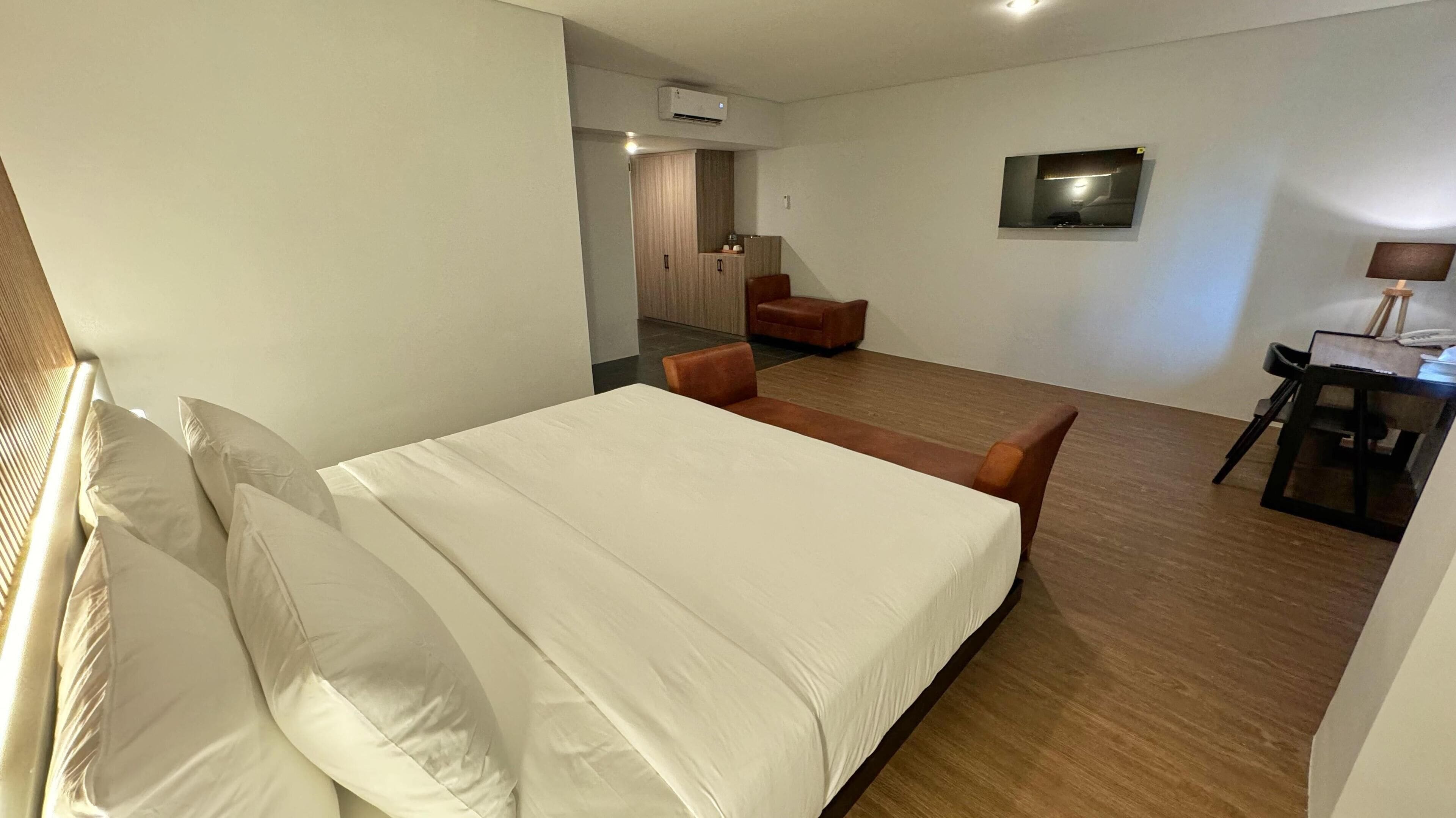 A modern hotel room with a large bed, a desk, a chair, and a TV.