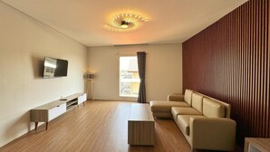 A modern living room with a flat-screen TV, a sofa, a coffee table, and a wooden floor. - Chara Hotel (Bandung)