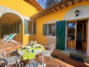 A patio with a table set for two, surrounded by white metal chairs, a yellow tablecloth, and a vase of flowers. - Il Frutteto by Interhome (Montescudaio)