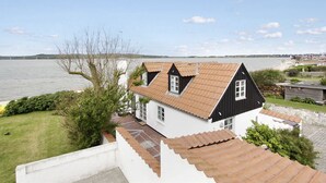 A coastal house with a white facade and brown roof tiles, overlooking a body of water and a distant shoreline. - "Pauliina" - 10m to the fjord by Interhome (Roslev)