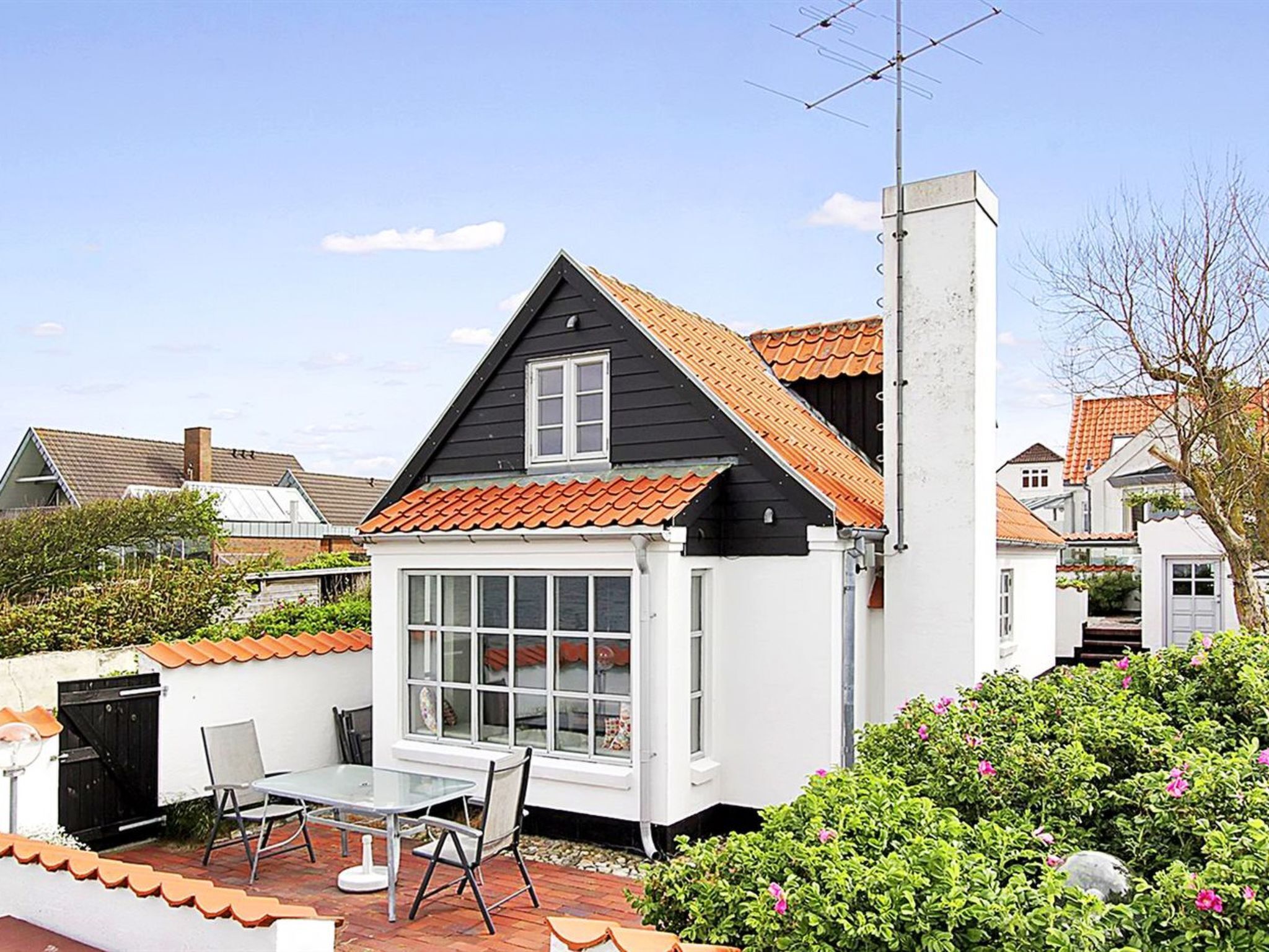 Une maison avec un toit noir, des murs blancs et un petit patio avec une table et des chaises.
