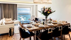 A modern dining area with a view of the ocean, a large window, and a chandelier. - Chic Apartment w Amazing Views Dunmore Luxe (Cape Town)