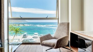 A room with a large window overlooking a coastal view, a chair, and a wooden floor. - Chic Apartment w Amazing Views Dunmore Luxe (Cape Town)