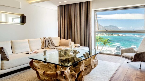 A modern living room with a glass coffee table, a sofa, and a view of the ocean. - Chic Apartment w Amazing Views Dunmore Luxe (Cape Town)