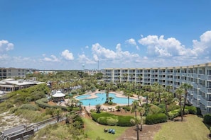 A hotel with a swimming pool surrounded by greenery, a parking area, and a multi-story building with balconies.