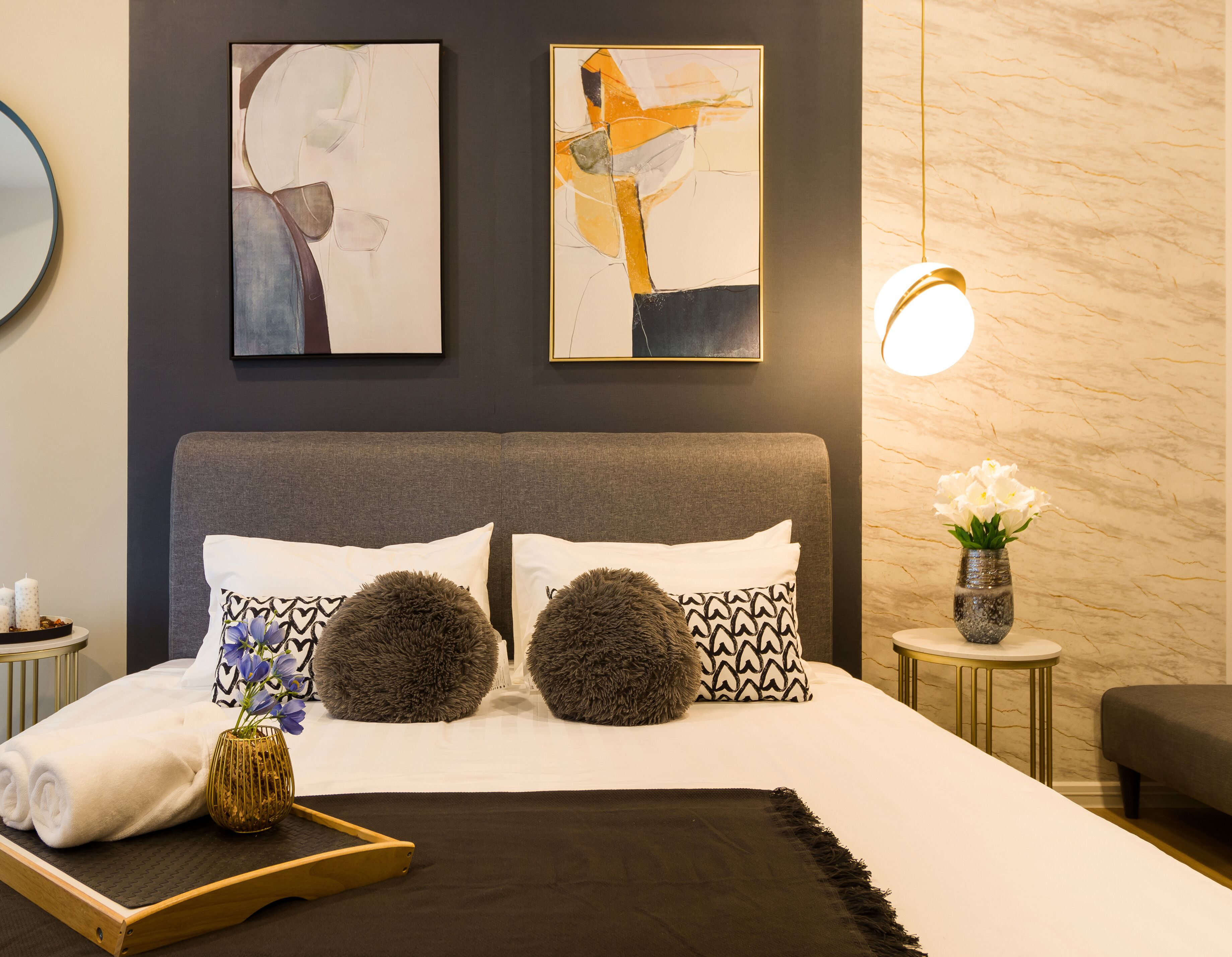 Et moderne hotelværelse med en stor seng, to bløde puder, et natbord med en vase blomster og abstrakt kunst på væggen.