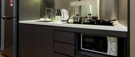 A modern kitchen with a built-in refrigerator, a sink, a kettle, a stove, and a microwave.