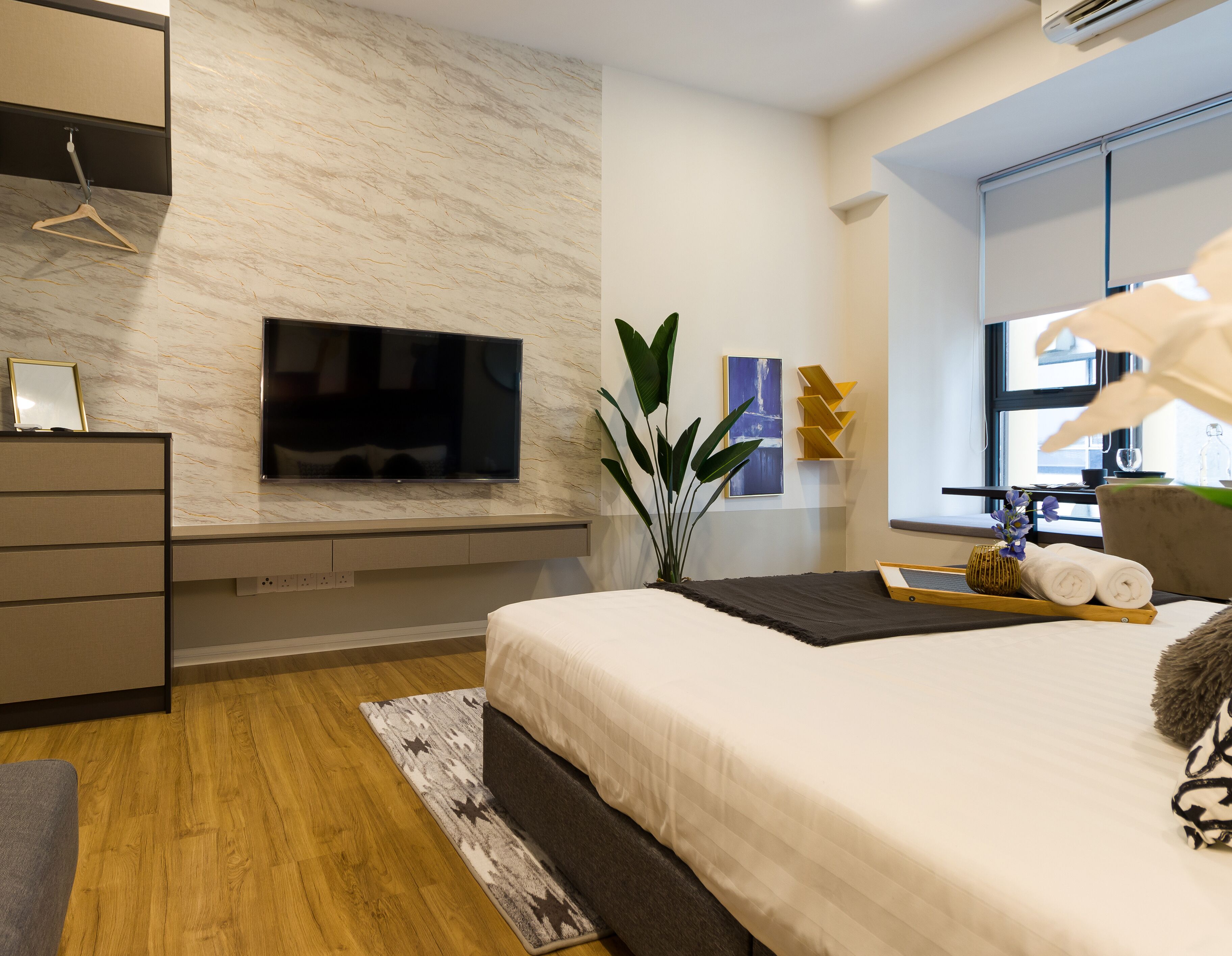 Ein modernes Schlafzimmer mit einem großen Bett, einem an der Wand montierten Fernseher, einem Schreibtisch mit Stuhl und einem Fenster mit Blick.