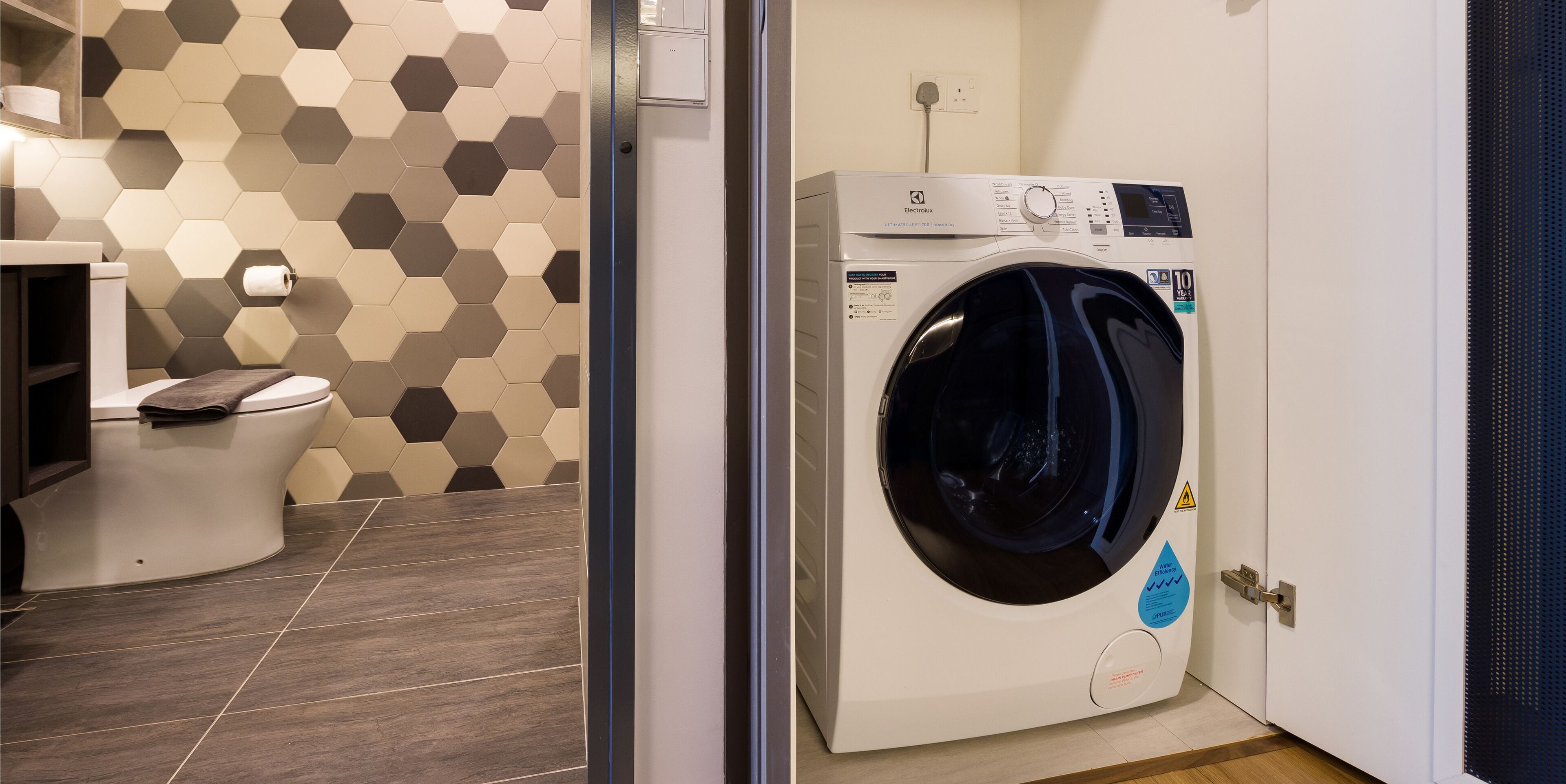 A compact bathroom with a toilet, a washing machine, and a hexagonal patterned wall.