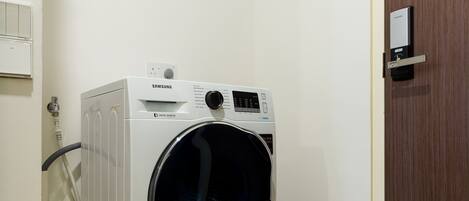 Una lavadora digital con tecnología Inverter Eco-Bubble de Samsung en una habitación con una puerta de madera y pared blanca.
