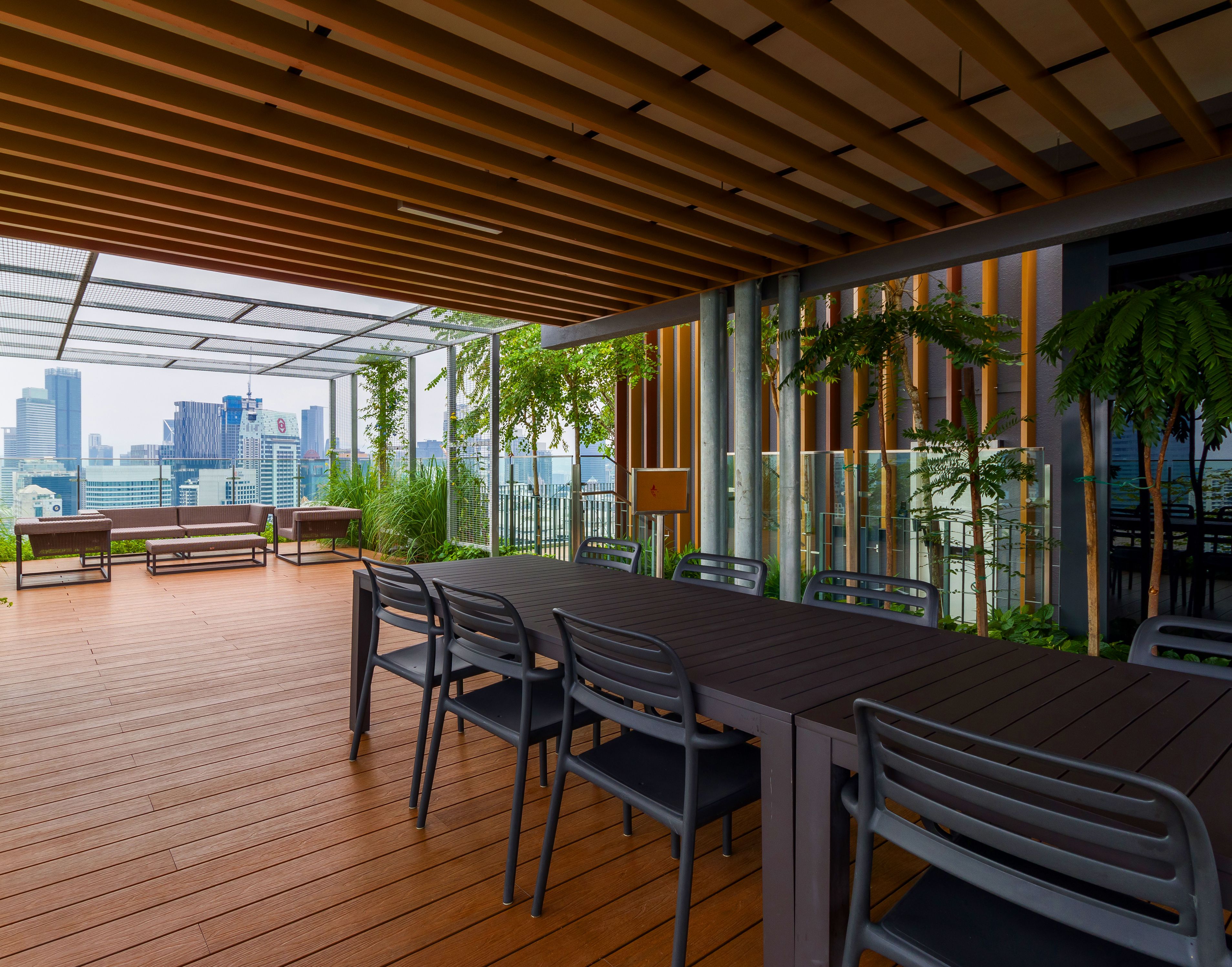 Una terraza exterior con piso de madera, una mesa de comedor con sillas, un banco y plantas en macetas.