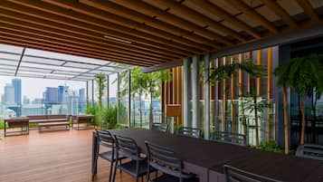 Una terraza exterior con piso de madera, una mesa de comedor con sillas, un banco y plantas en macetas.
