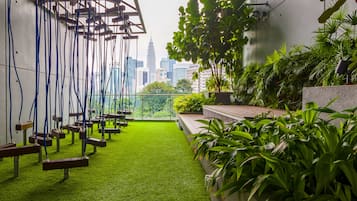 Un jardín en la azotea con columpios, follaje y vistas del horizonte urbano.