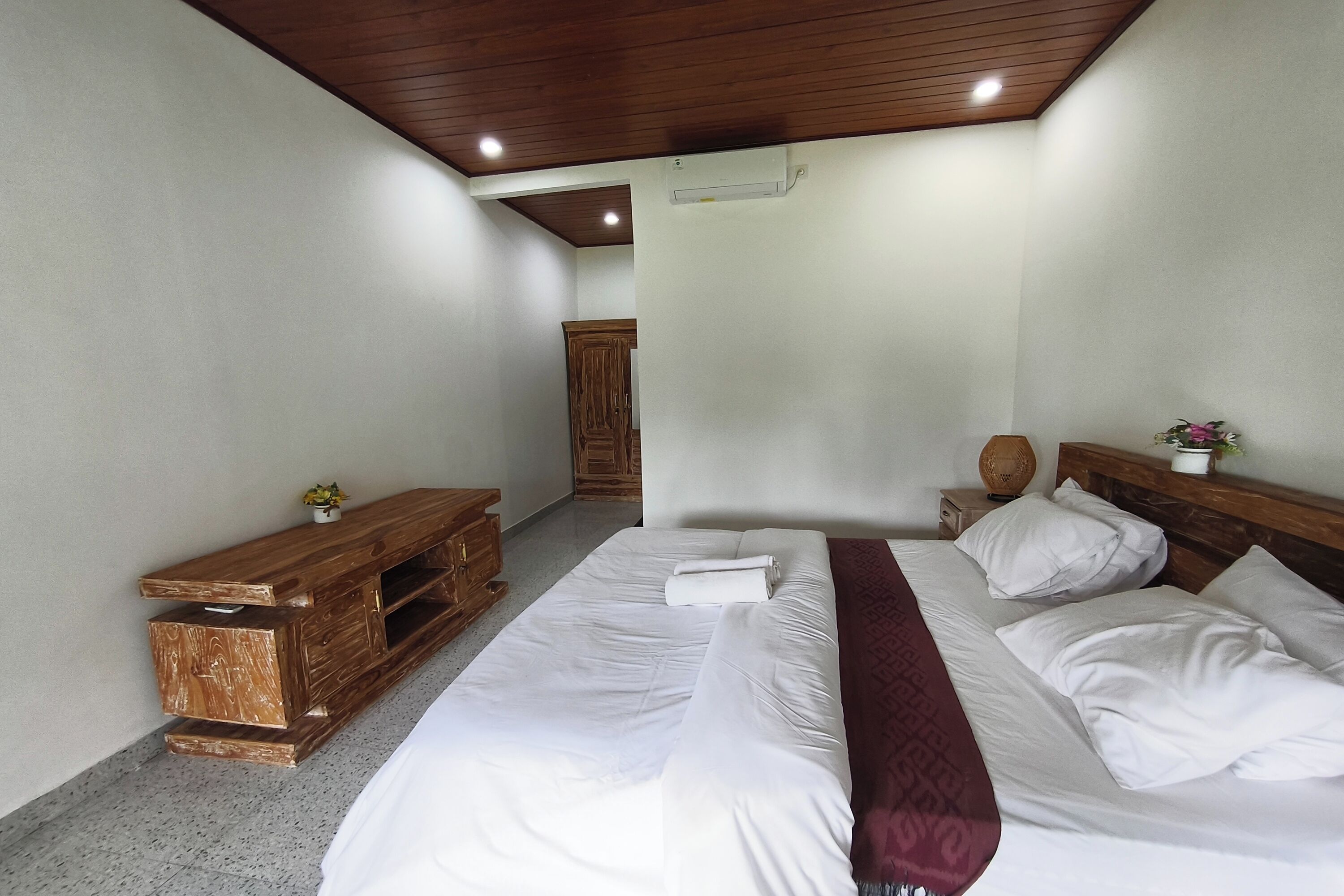 A bedroom with a wooden headboard, a bed with white linens, a wooden nightstand, and a small table with a vase.