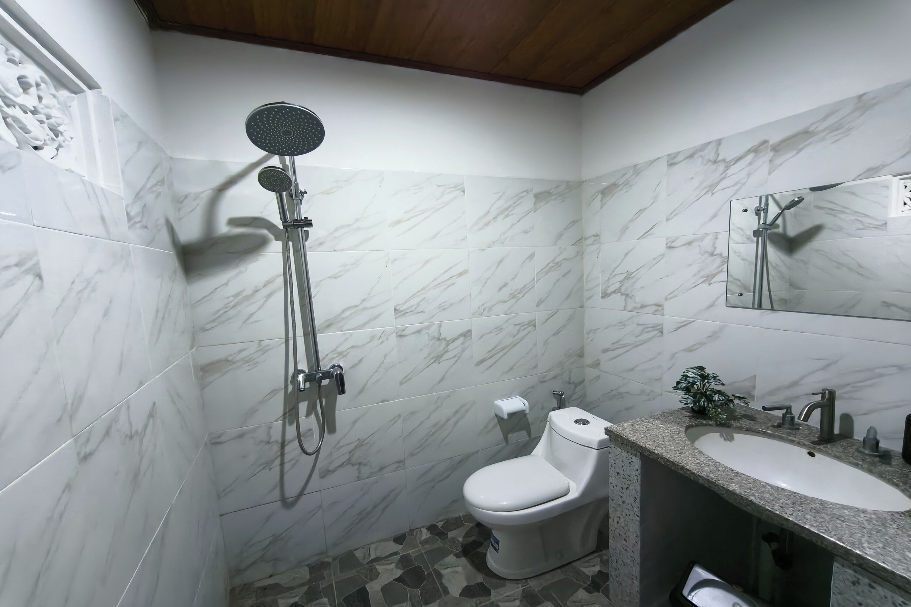 A bathroom with a shower, toilet, sink, and marble tiles.