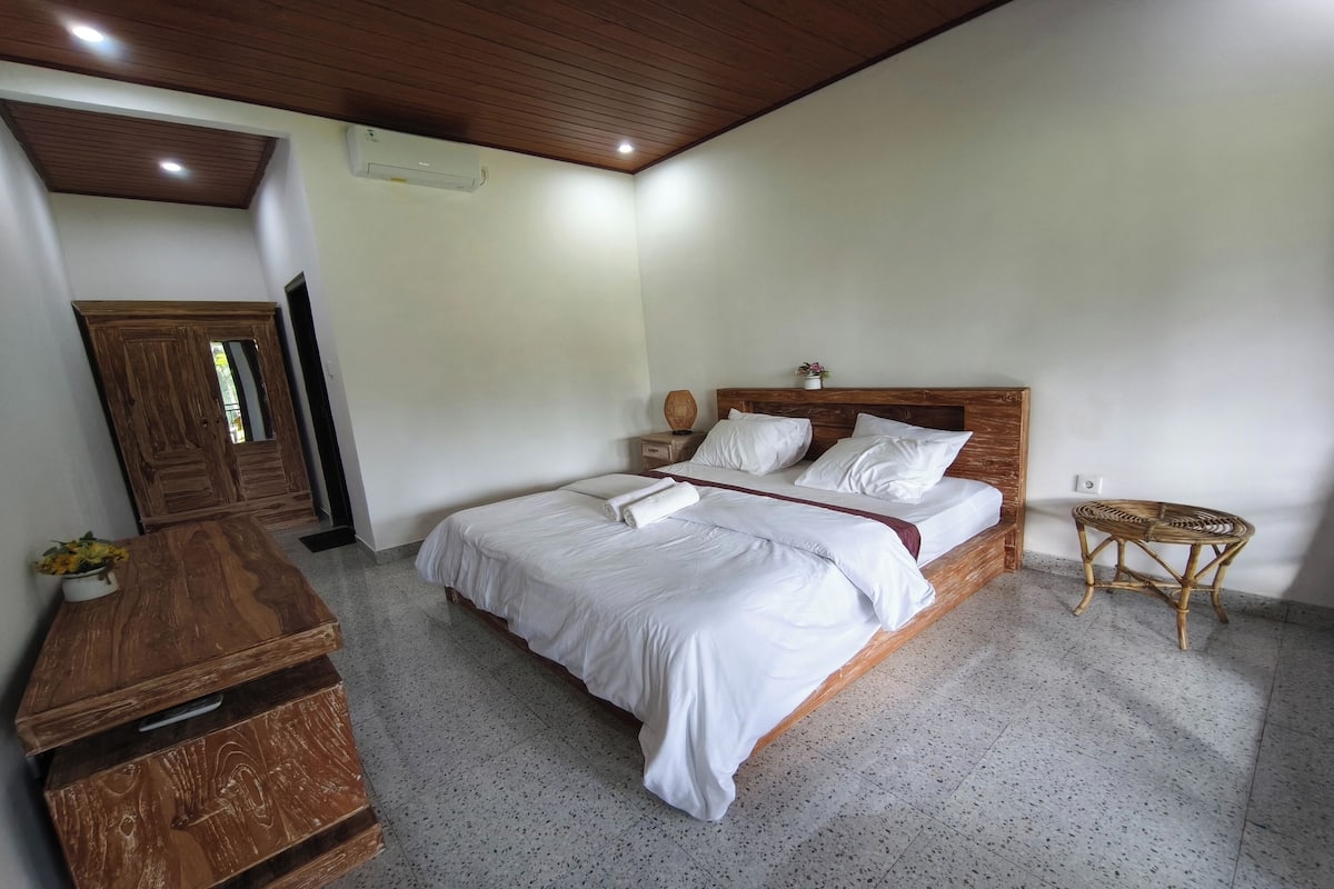 A bedroom with a wooden bed, a bedside table, a small wicker side table, and a wardrobe.
