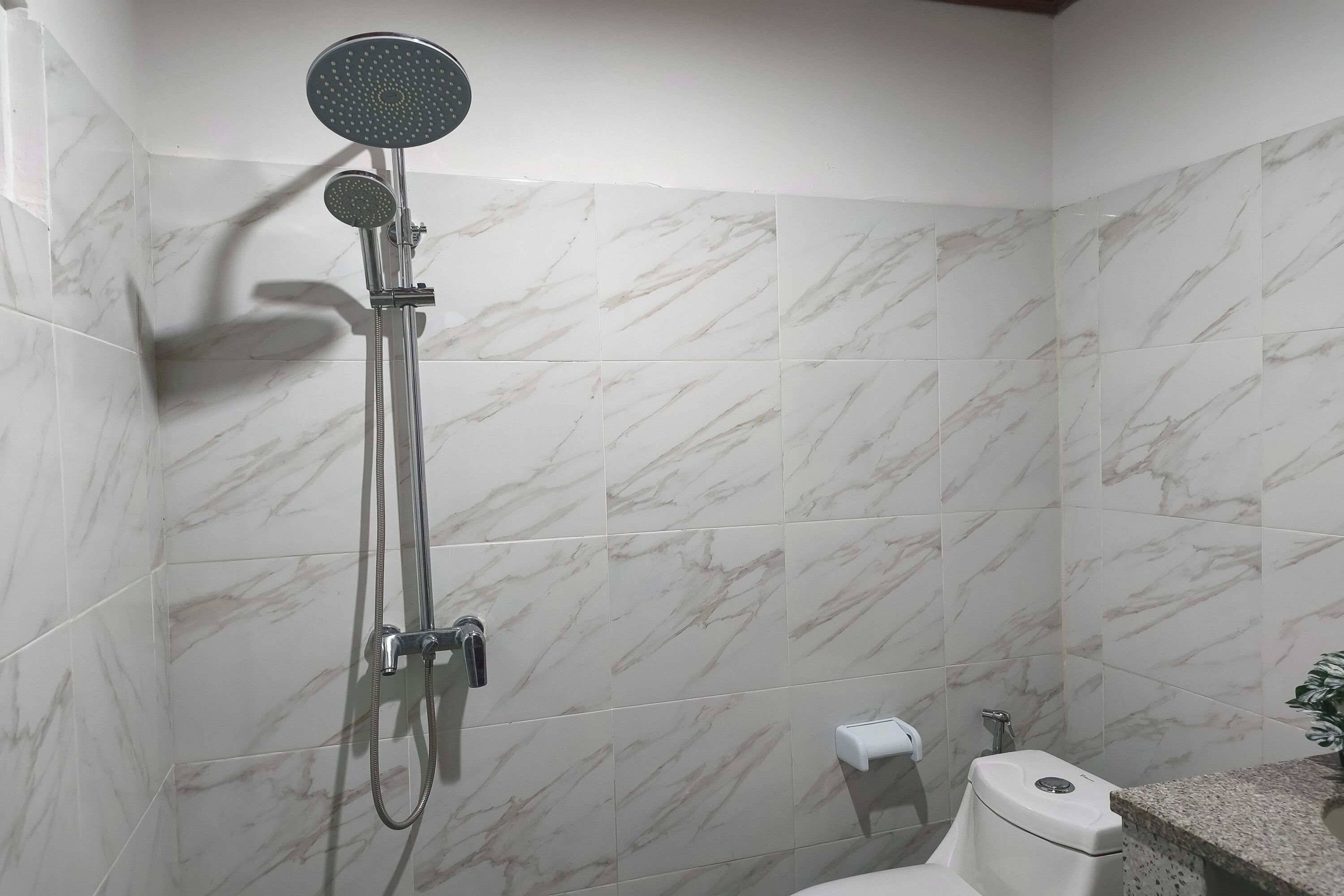 Un baño con ducha, inodoro y azulejos de mármol.