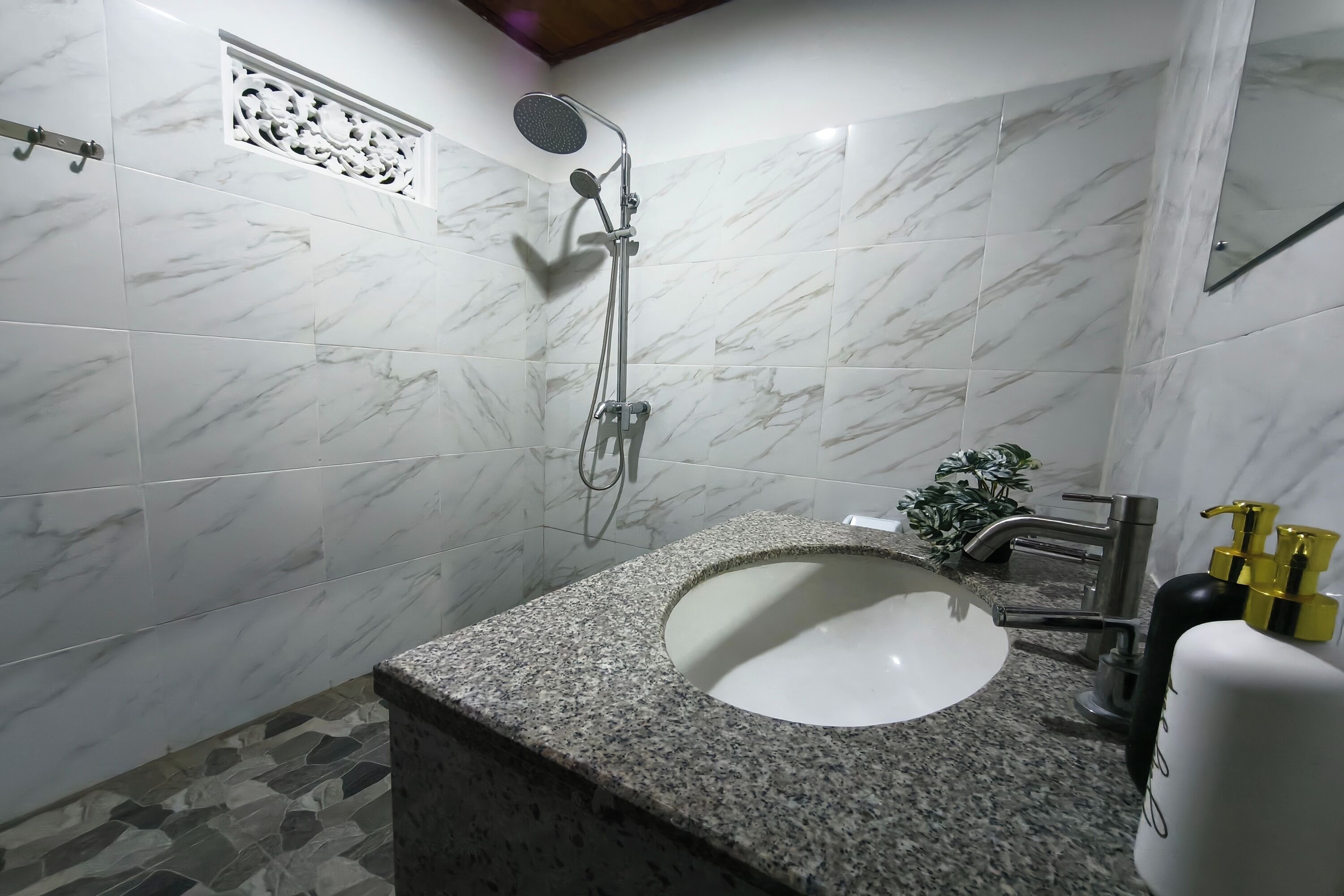 A bathroom with a marble shower, a granite sink, and a small plant.
