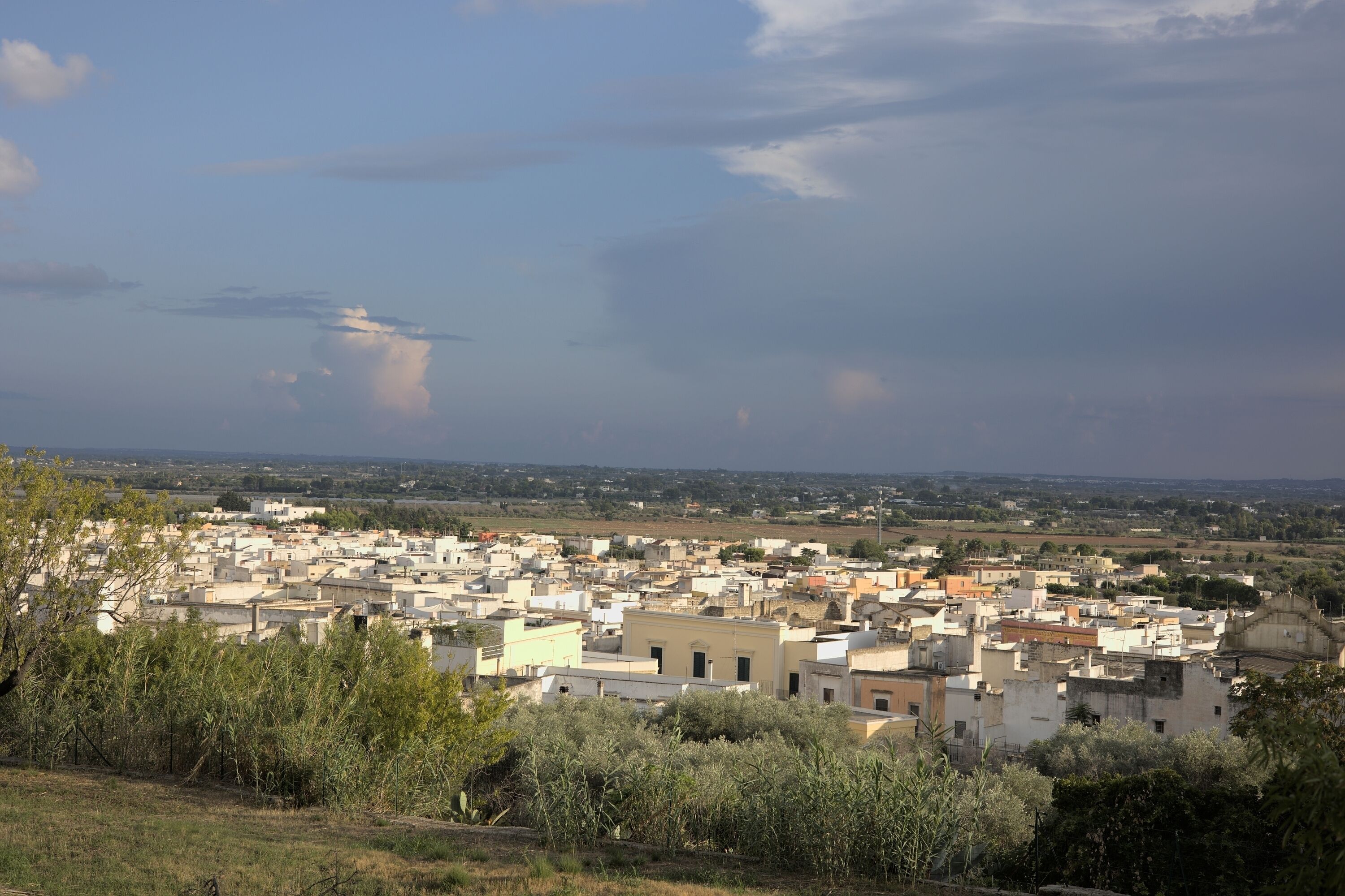 A densely packed urban area with numerous buildings, some with flat roofs and others with sloped roofs, under a partly cloudy sky.
