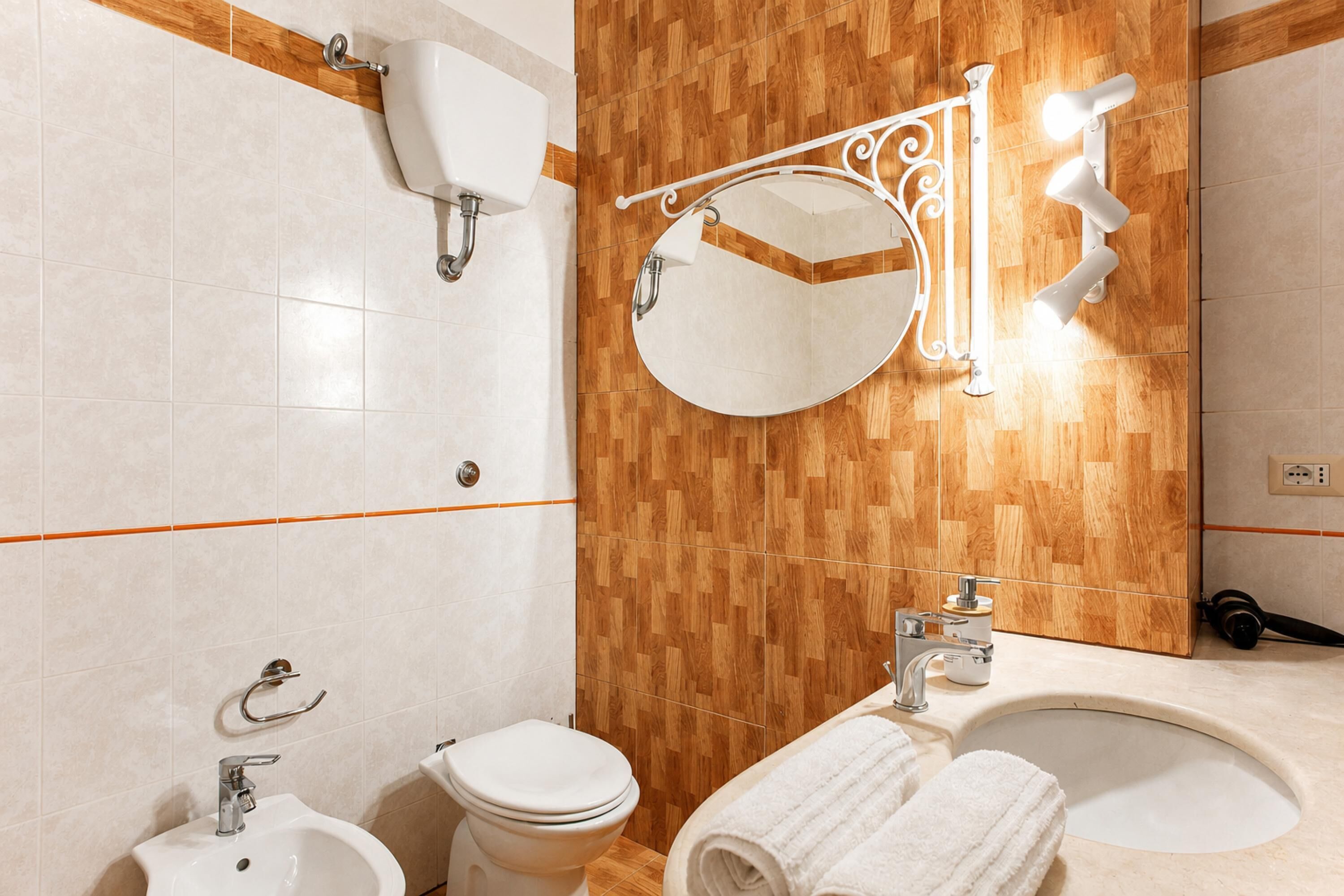 Un baño con lavamanos, inodoro, bidé, espejo y paneles de madera en la pared.