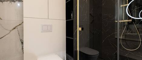 A modern bathroom with a white toilet, a glass-enclosed shower area, and marble walls.