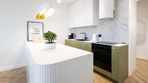 A modern kitchen with white cabinetry, a marble backsplash, and a central island with a potted plant. - Menta Panorama Apartment Widok na Oper Nova Brd (Bydgoszcz)
