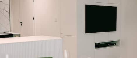 Una cucina moderna con TV integrata, mobili bianchi e una parete di fondo in marmo.