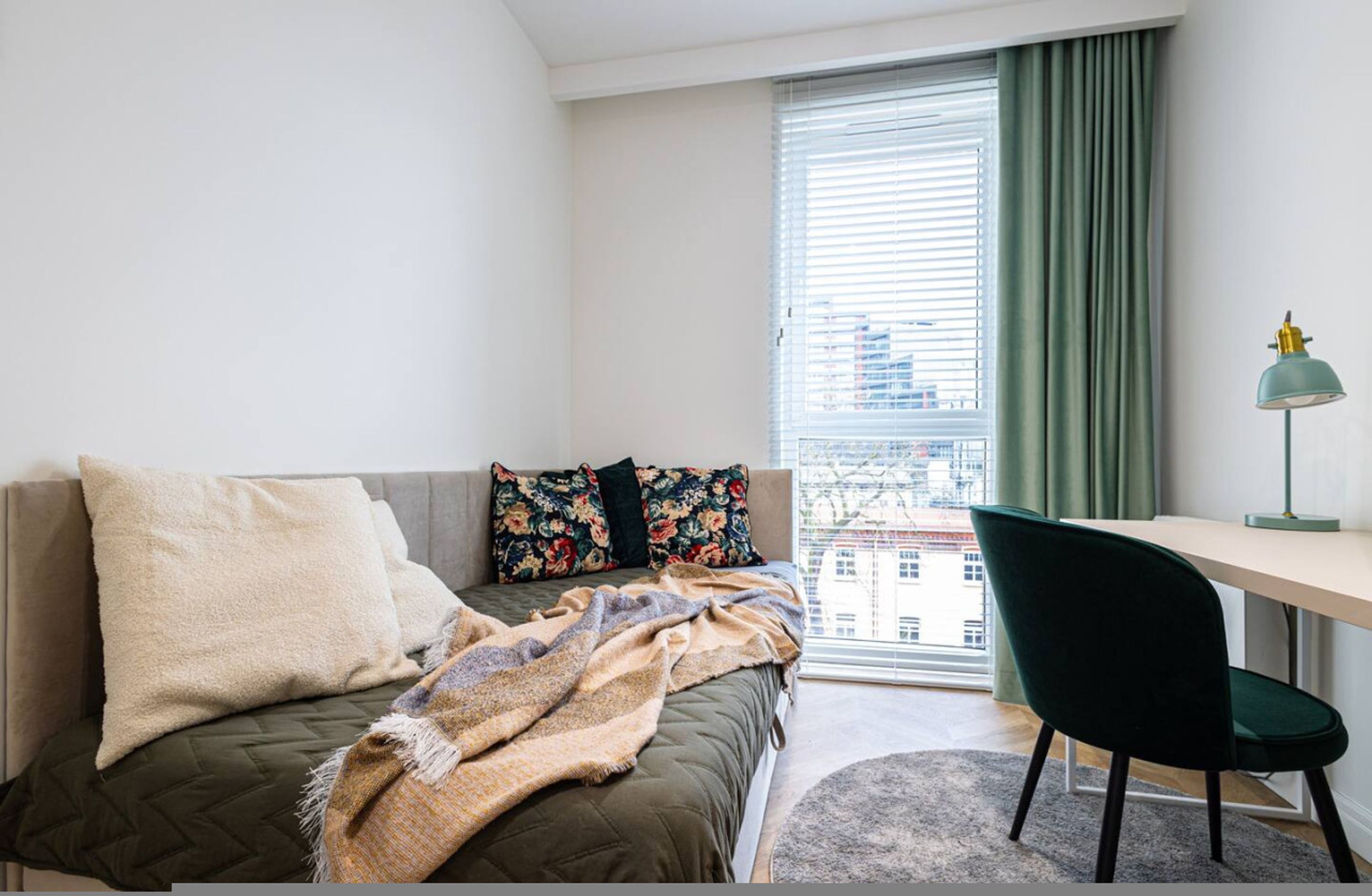 A bedroom with a bed, a desk, a chair, and a window with curtains.