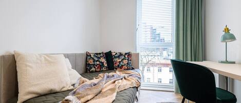 A bedroom with a bed, a desk, a chair, and a window with curtains.