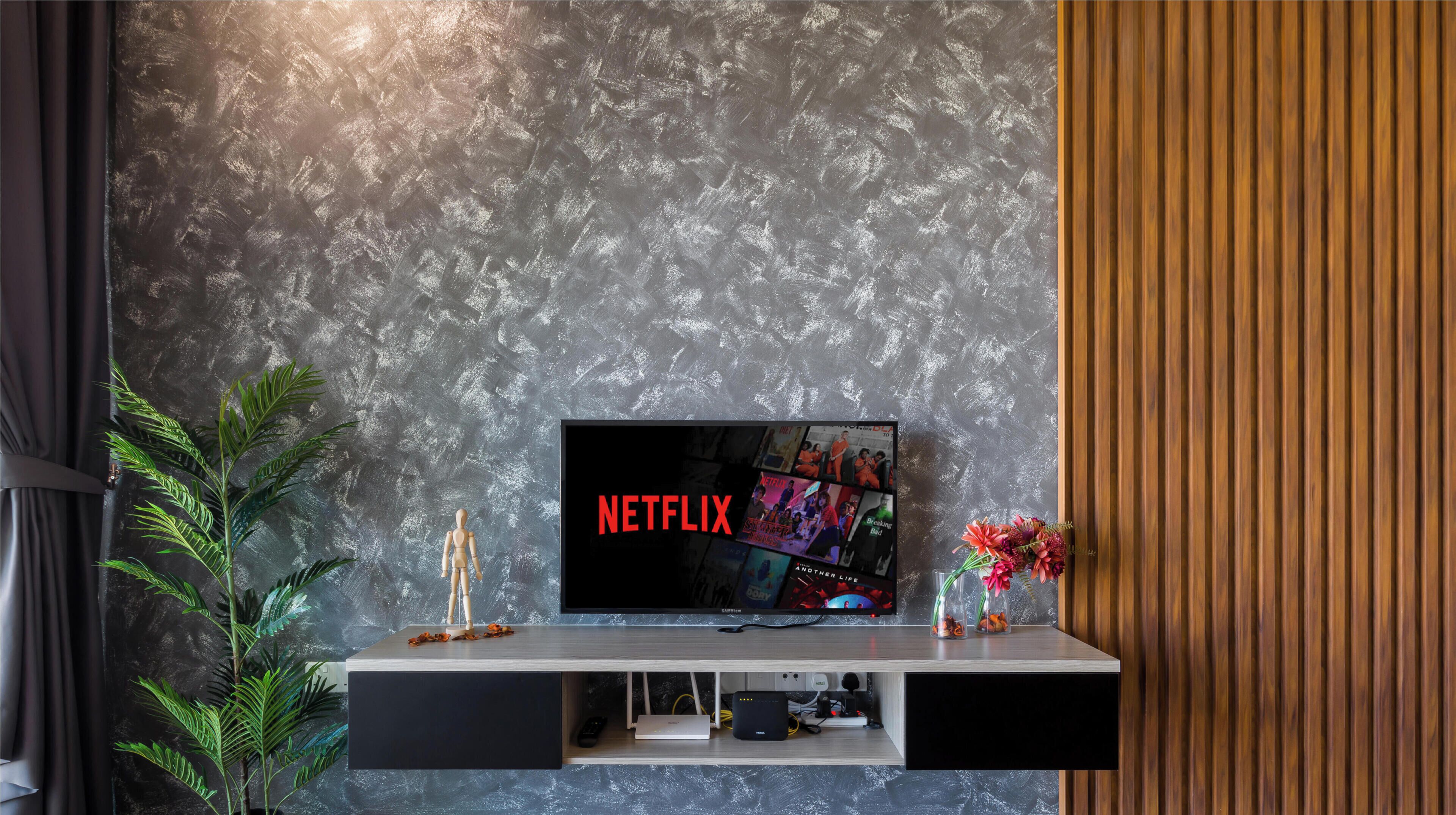 A modern living room with a flat-screen TV on a wooden TV stand, a plant, and a vase with flowers.