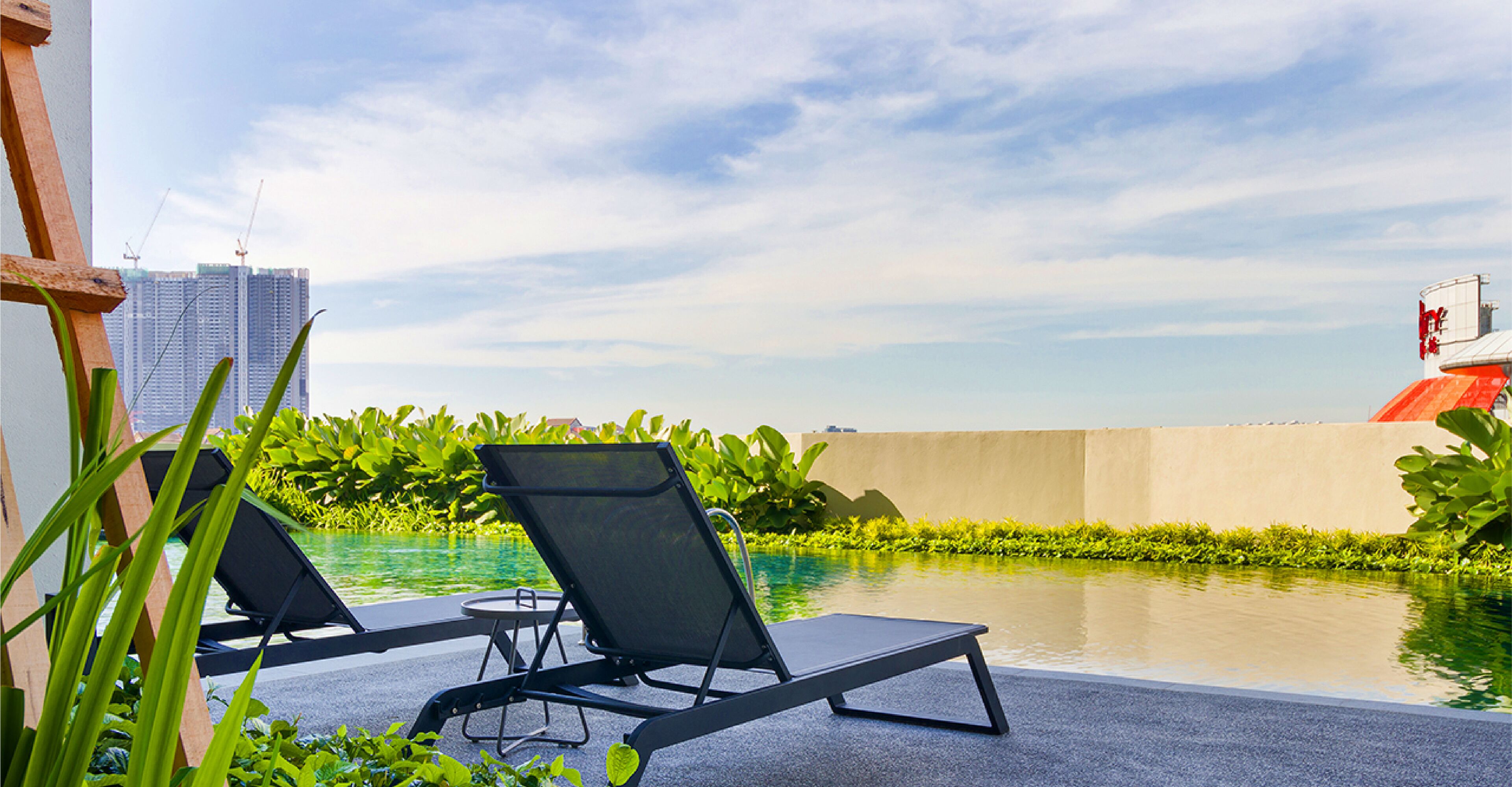 A rooftop pool area with two lounge chairs, a concrete barrier, and a view of city buildings.