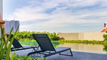 A rooftop pool area with two lounge chairs, a concrete barrier, and a view of city buildings.