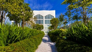 Un bâtiment moderne à la façade symétrique, entouré d’une végétation luxuriante et doté d’un chemin de gravier menant à l’entrée.