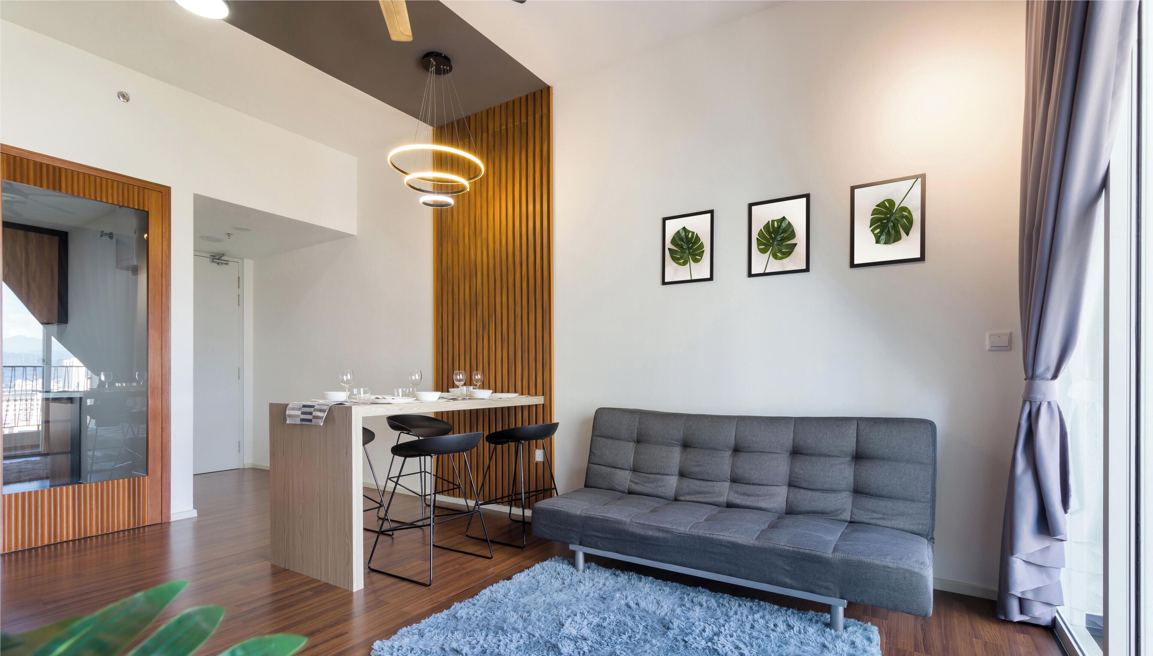 Uma sala de estar moderna com um sofá cinzento, uma mesa de jantar de madeira com cadeiras e três quadros de plantas na parede.