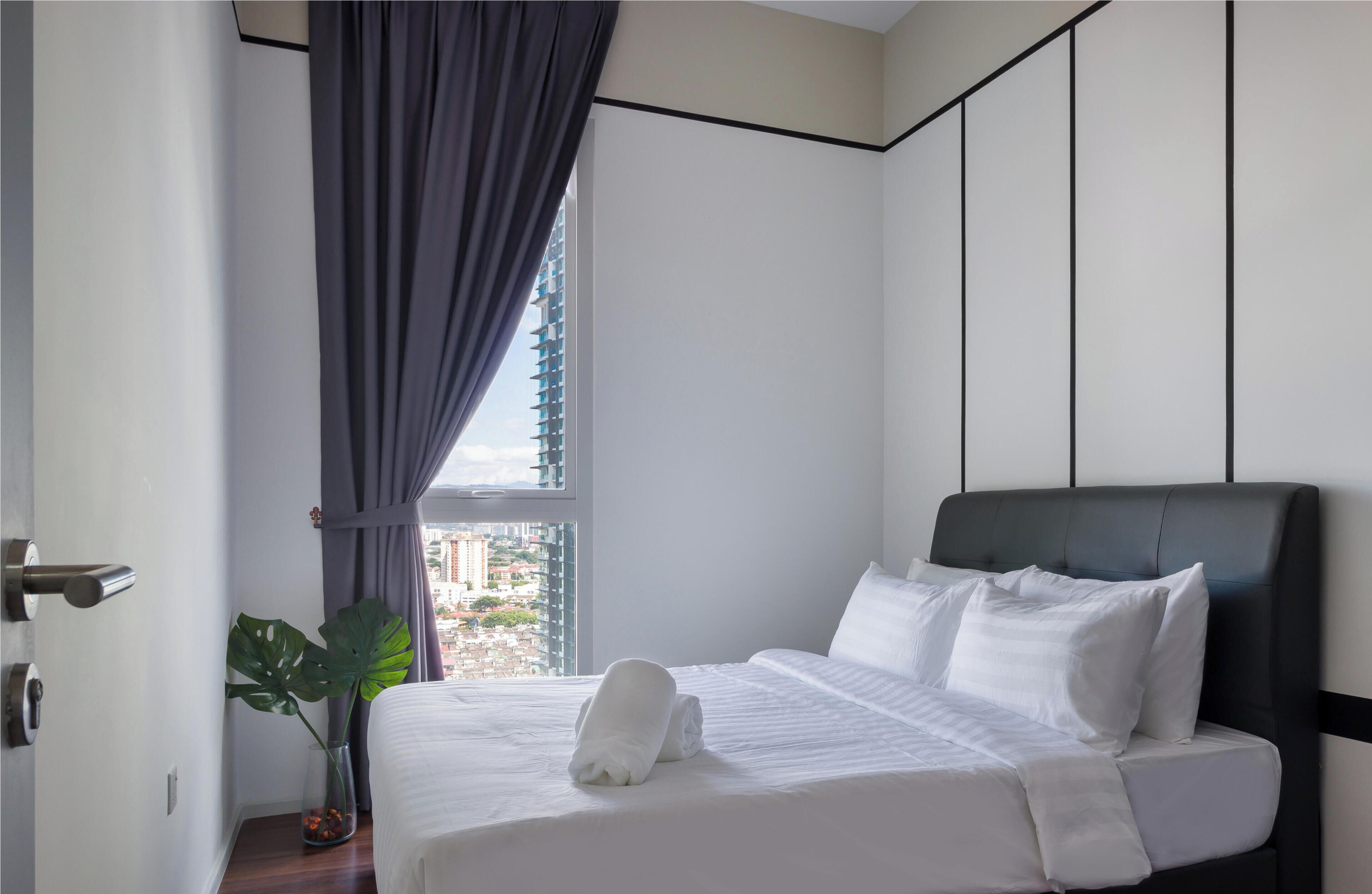 Hotellihuone, jossa on sänky, ikkuna verhoilla, huonekasvi ja näkymä kaupunkimaisemaan.