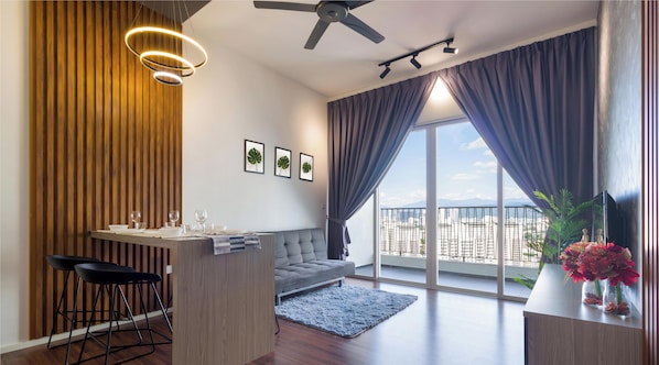 A modern living room with a sofa, dining table, and chairs, a balcony with a view, and a ceiling fan.