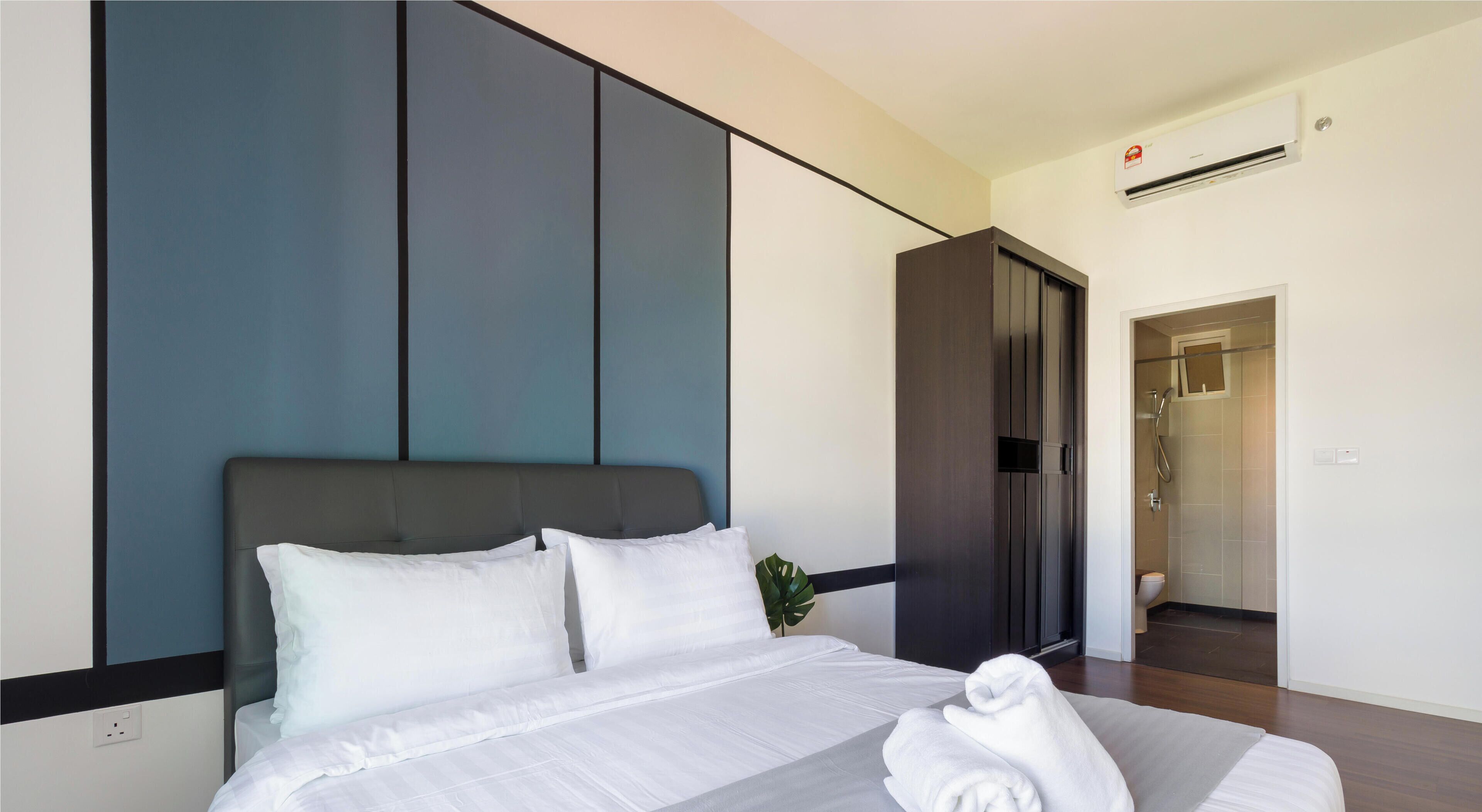 Una habitación de hotel moderna con una cama grande, un cabecero oscuro, una planta y una puerta que da a un baño.
