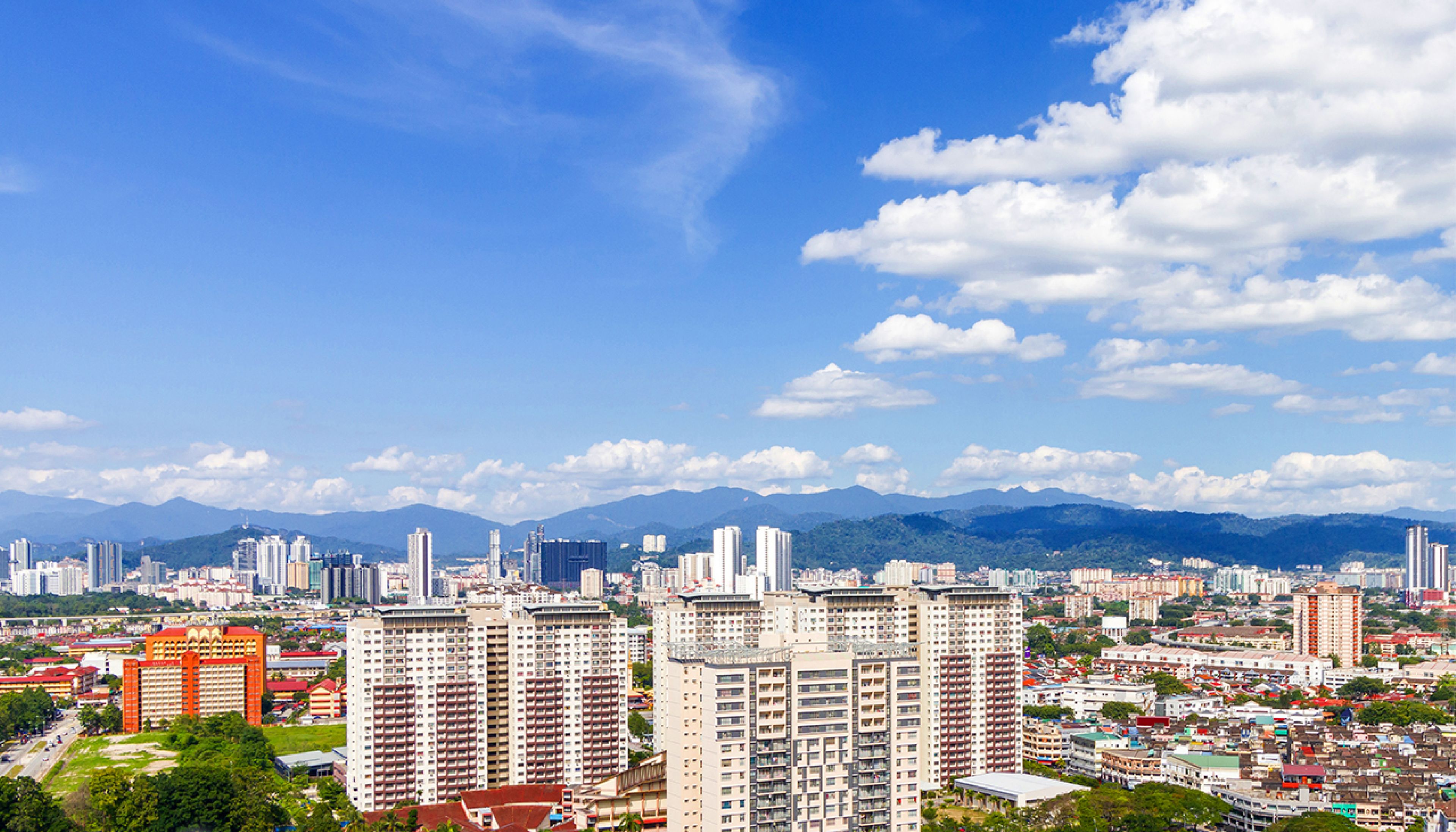 A cityscape with high-rise buildings, a clear sky, and mountains in the background.