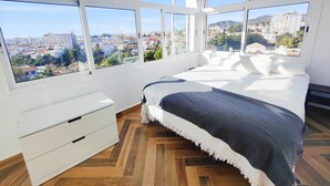 A bedroom with a large window, a bed, a white dresser, and a herringbone-patterned wooden floor. - AP393 LOS ALMENDROS (Nerja)