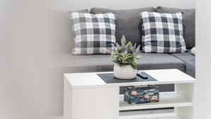 A modern living room with a white coffee table, a grey sofa with checkered cushions, and a small potted plant.