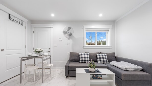 A modern living room with a grey sofa, a white coffee table, and a dining area with a white table and chairs.