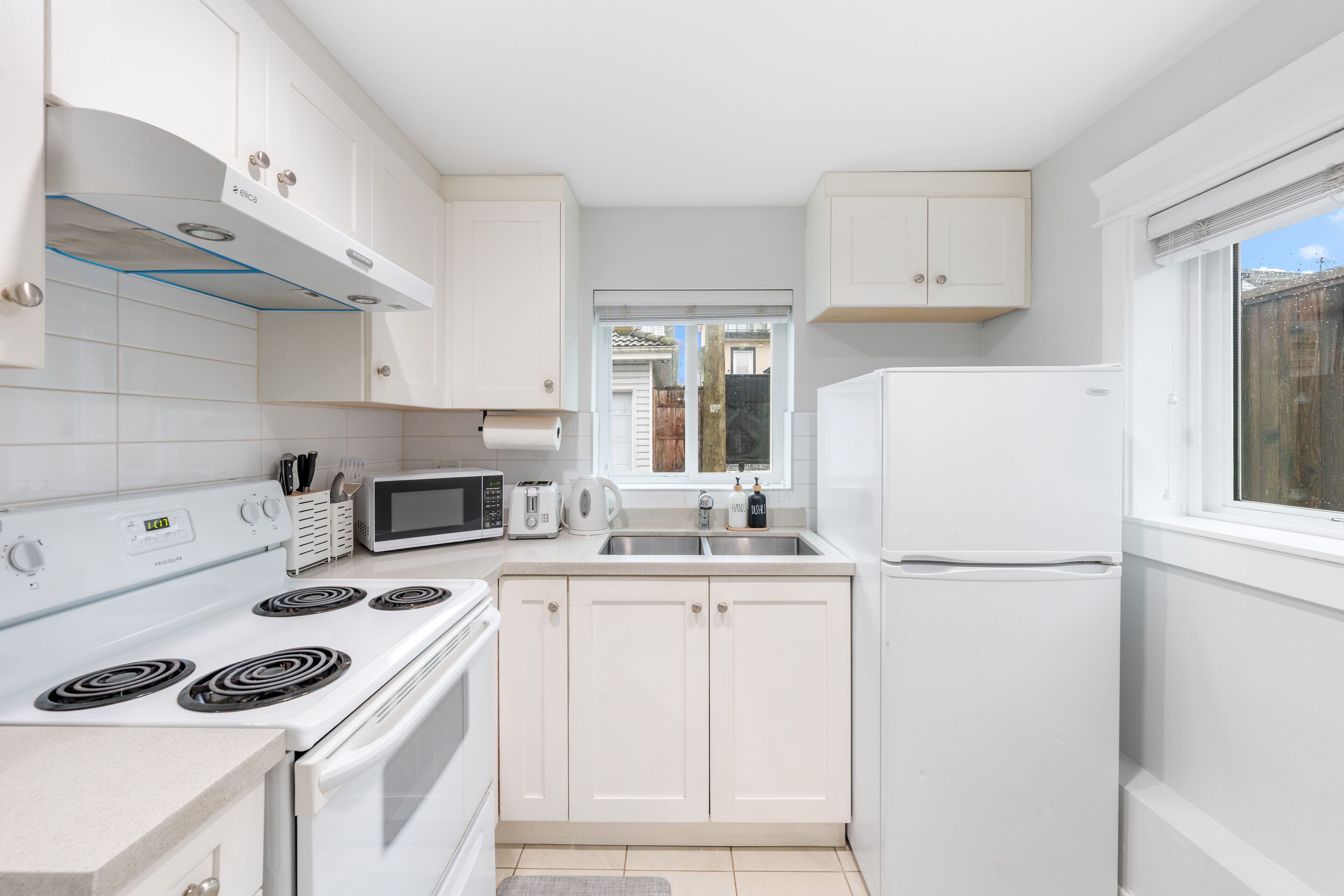 A modern kitchen with white cabinets, a stove, microwave, and a refrigerator.