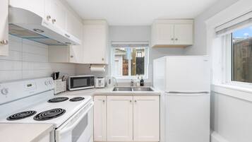 A modern kitchen with white cabinets, a stove, microwave, and a refrigerator.
