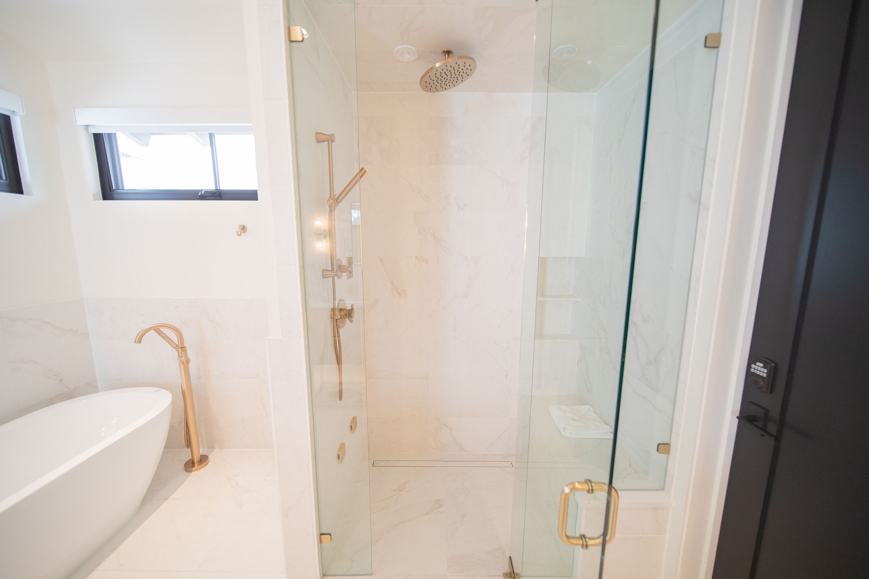 A modern bathroom with a freestanding bathtub, a glass-enclosed shower with a handheld showerhead, and a small window above the tub.